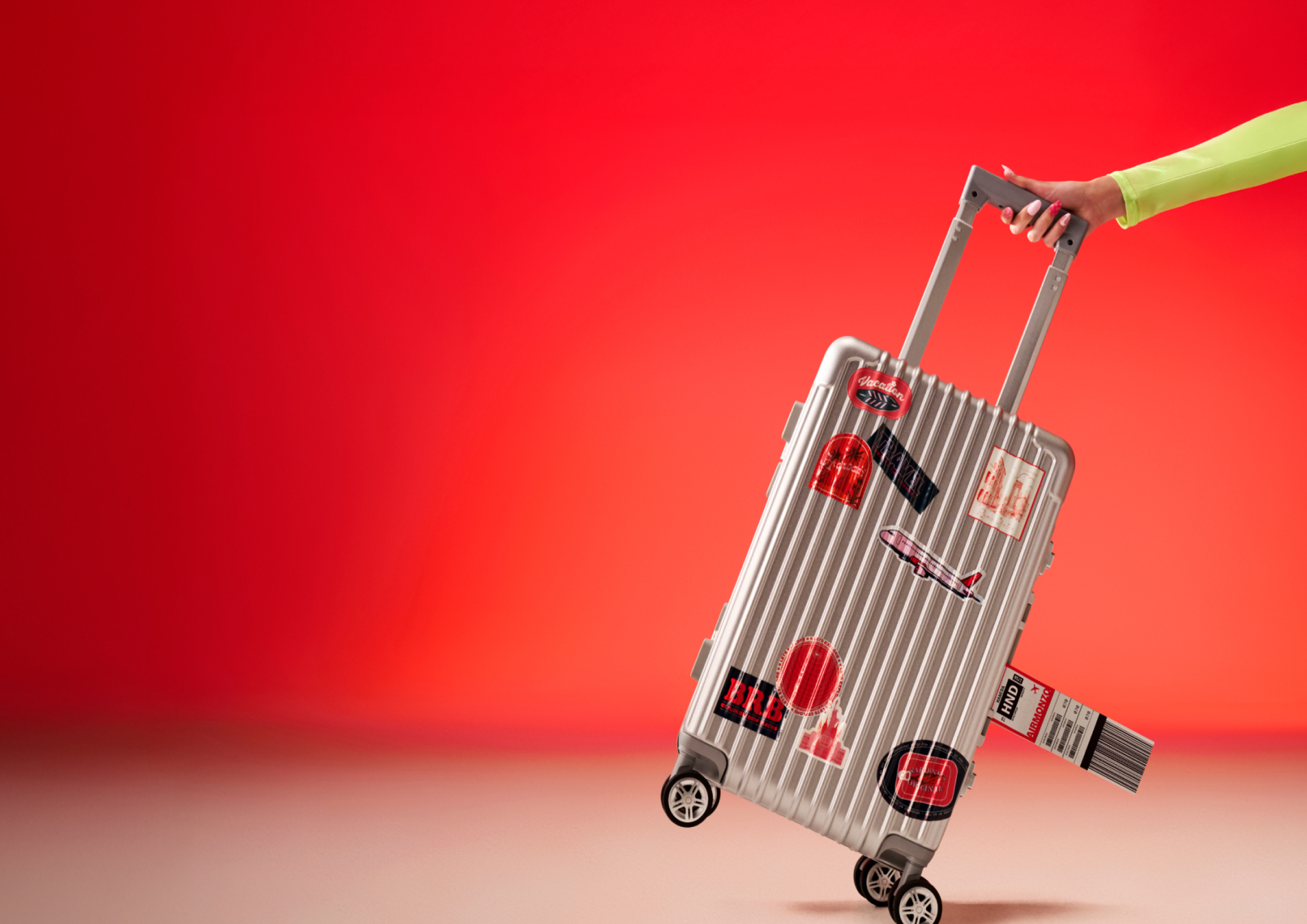 A person's hand holding a grey suitcase in front of a hot coral background