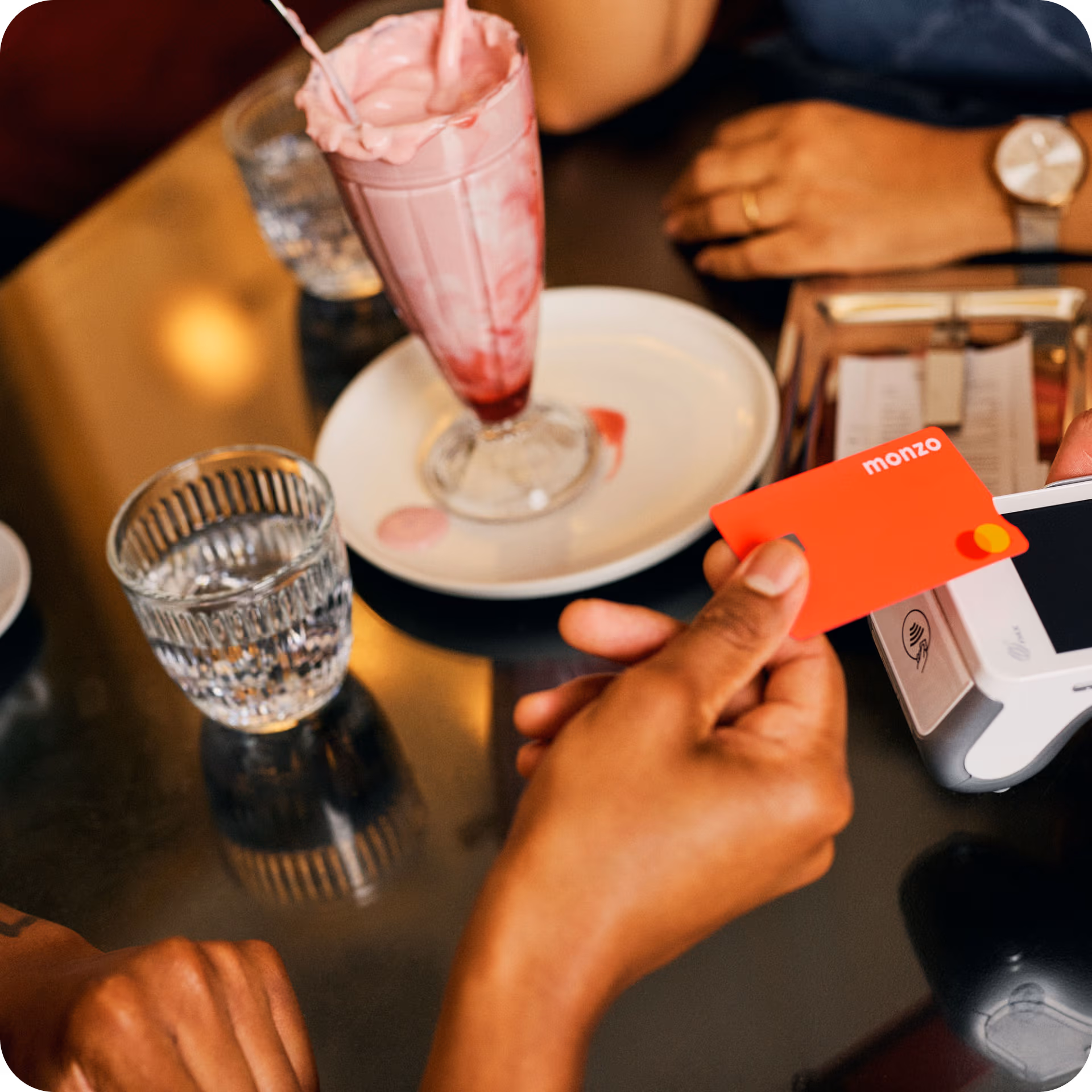 A person paying a bill at a restaurant table with their Monzo current account card
