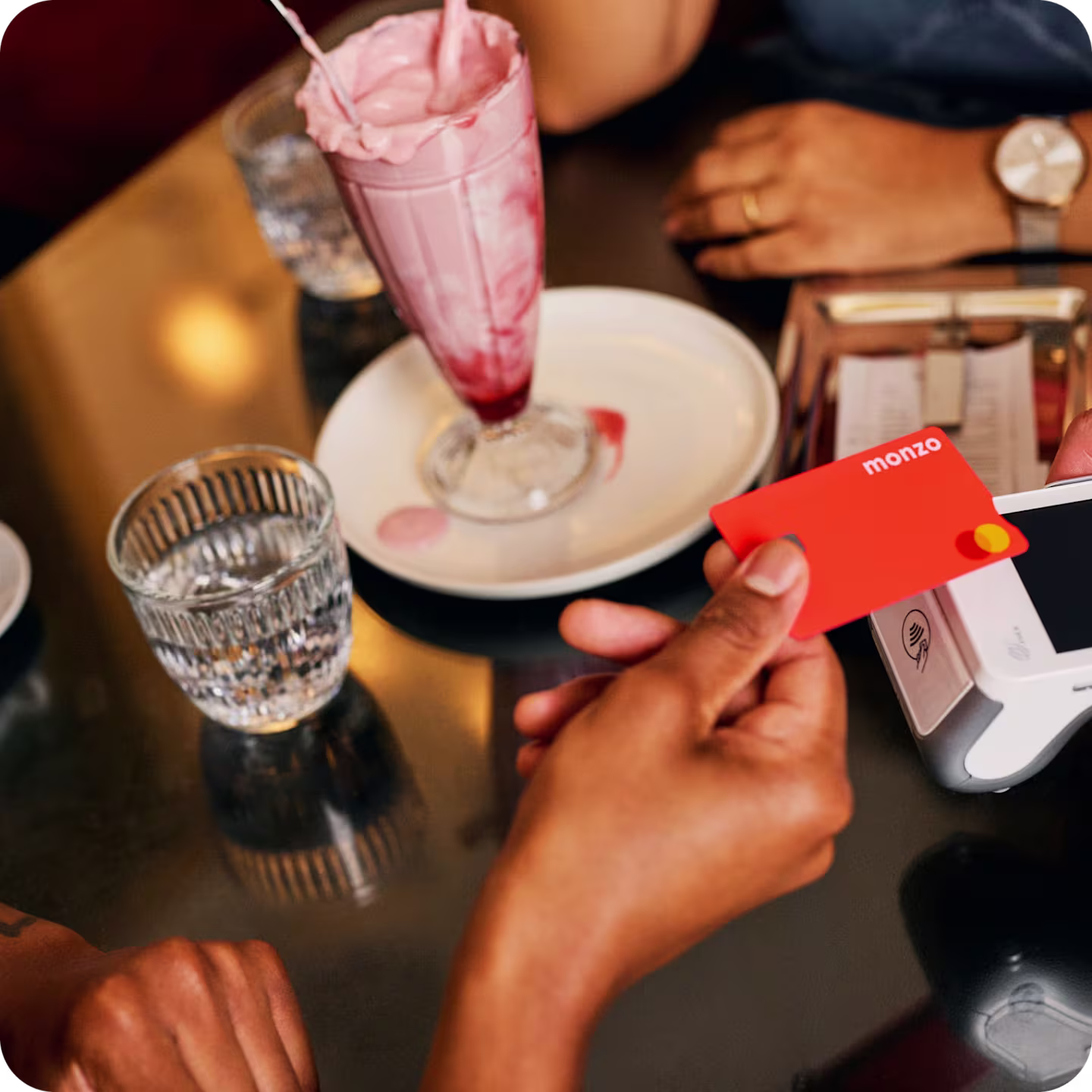 A person paying a bill at a restaurant table with their Monzo current account card