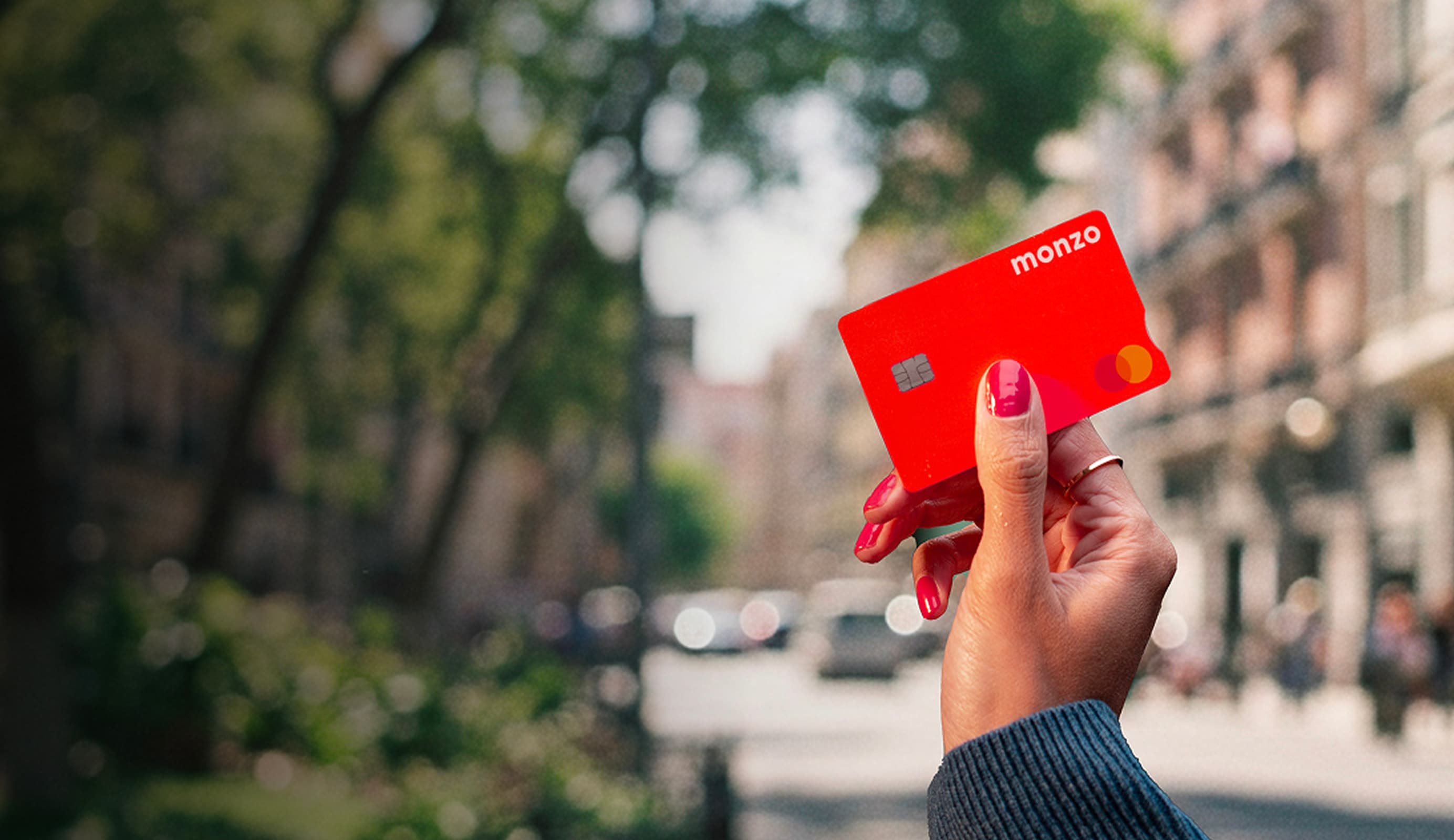 A person's hand holding a Monzo hot coral bank card with a visible chip