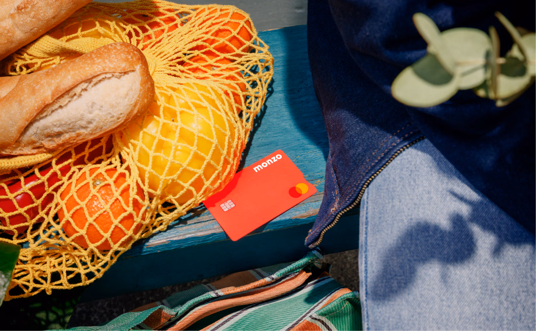A hot coral Monzo card on a bench next to some groceries.