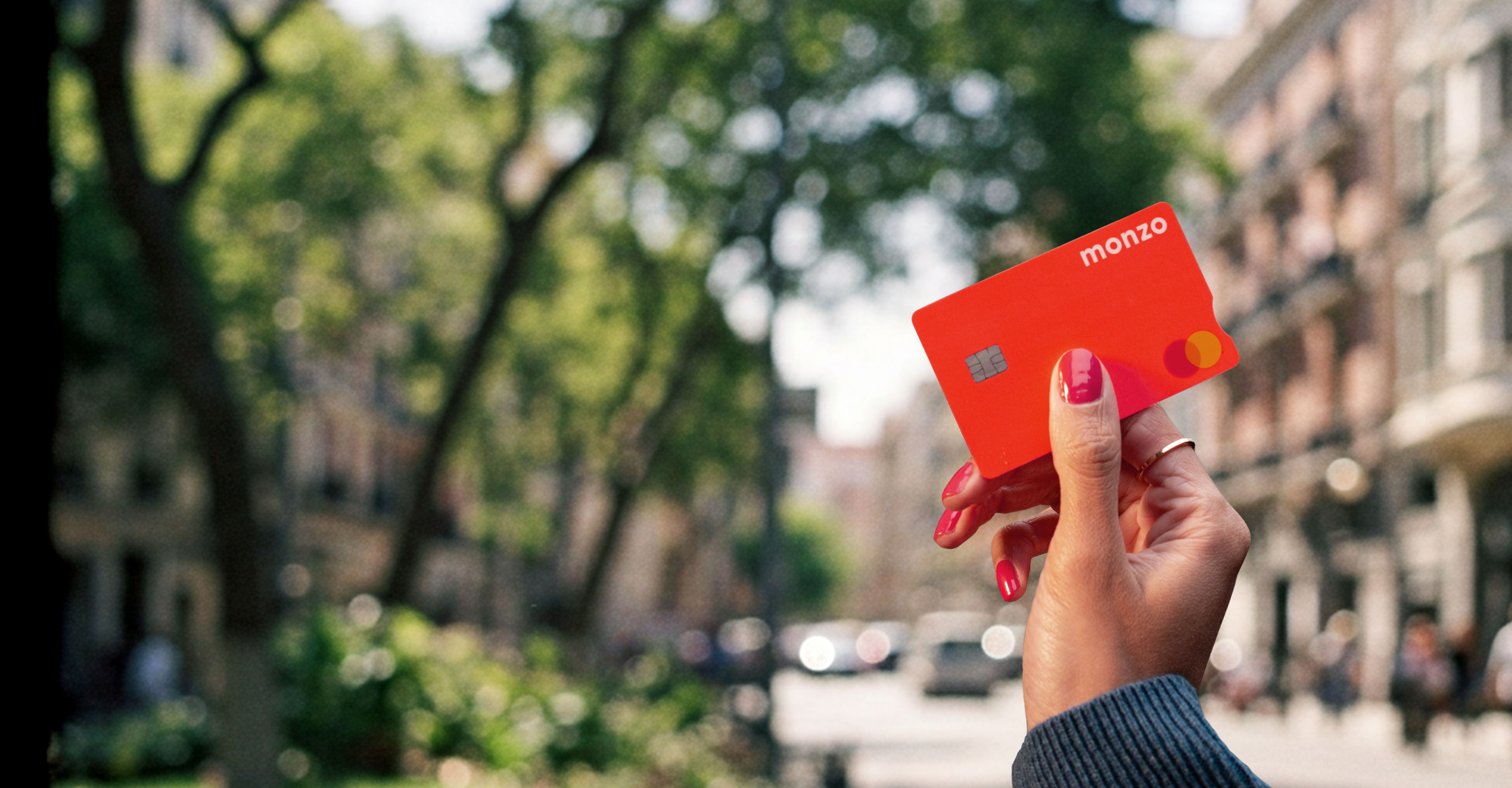 A person's hand holding a Monzo hot coral bank card with a visible chip