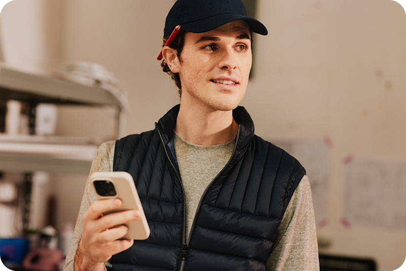 Tradesperson in work gear holding their phone and smiling, ready to manage their business on the go from a construction site.