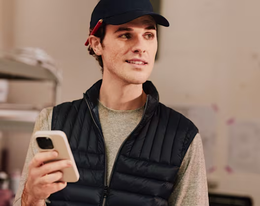 Tradesperson in work gear holding their phone and smiling, ready to manage their business on the go from a construction site.