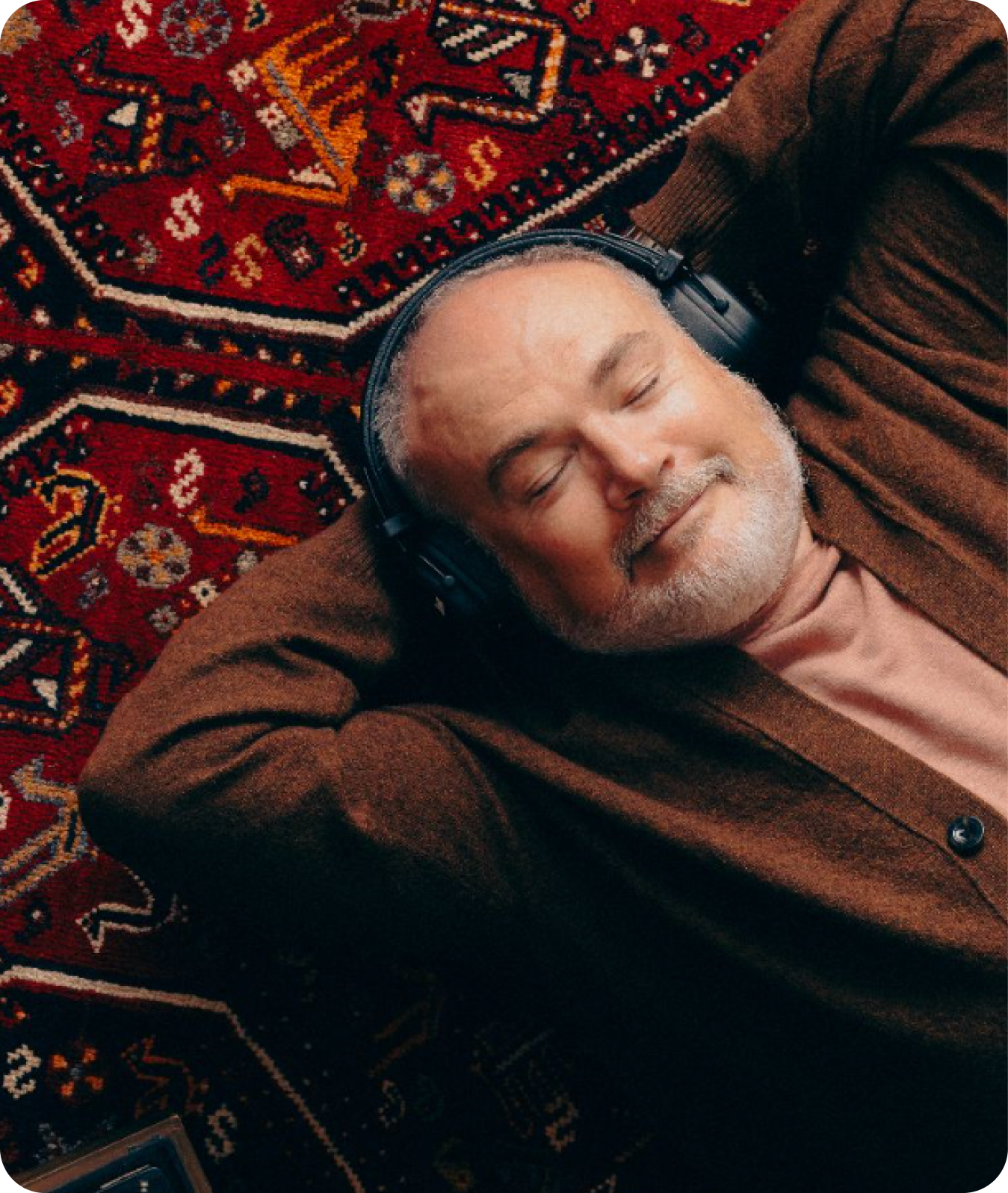 Photo of a man lying down on a red carpet, contentfully listening to music with overhead earphones.