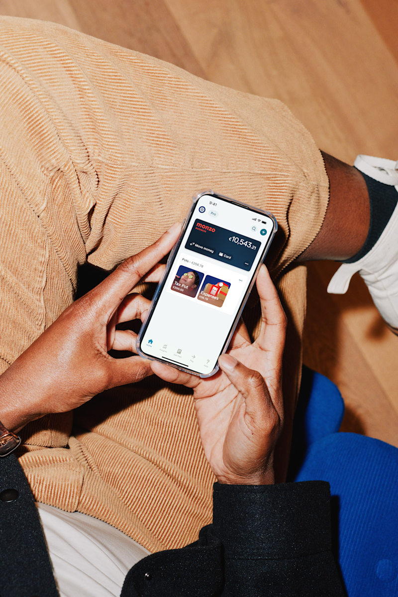 Person sitting down holding a smartphone, browsing an app with content tiles on the screen.