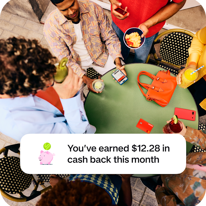 An overhead view of friends gathered around a green table with drinks and a Monzo card, overlaid with a notification celebrating $12.28 in cash back earned this month.