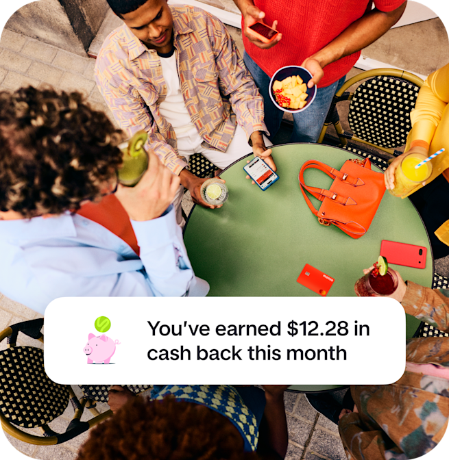 An overhead view of friends gathered around a green table with drinks and a Monzo card, overlaid with a notification celebrating $12.28 in cash back earned this month.