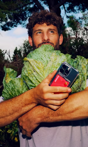A man holds very large lettuce. He's also got a phone in his hand with a Monzo bank card attached in the case.