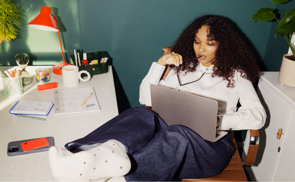 Woman in a home office with a laptop and feet up on a desk.