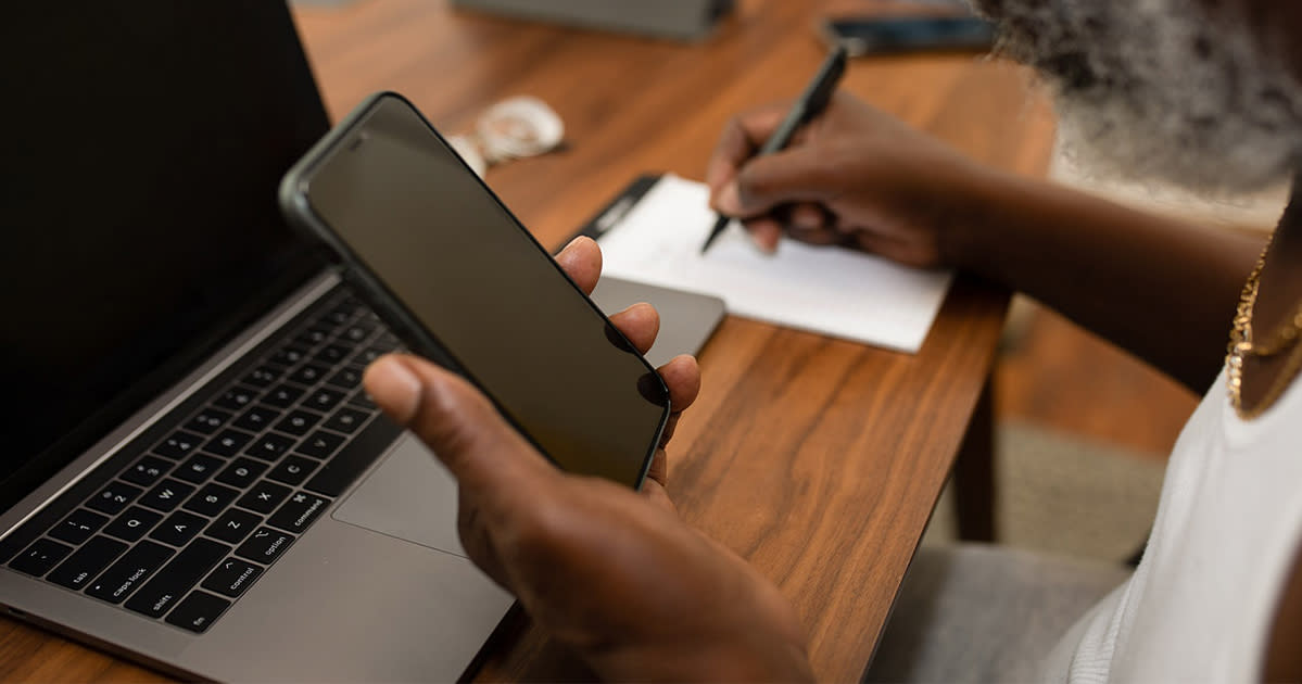 someone holding a phone and taking notes on a desk