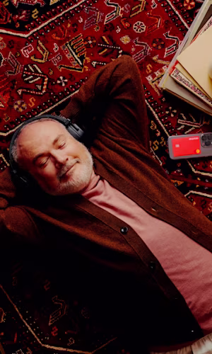 An arm reaches for a red, spiky apple hanging from a tree branch alongside regular red apples, against a cloudy blue sky