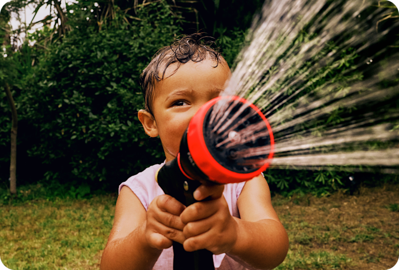 Little girl spraying shower hose in a garden