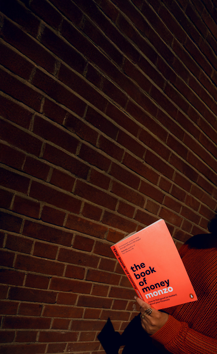 The Book of Money being held against a brick wall