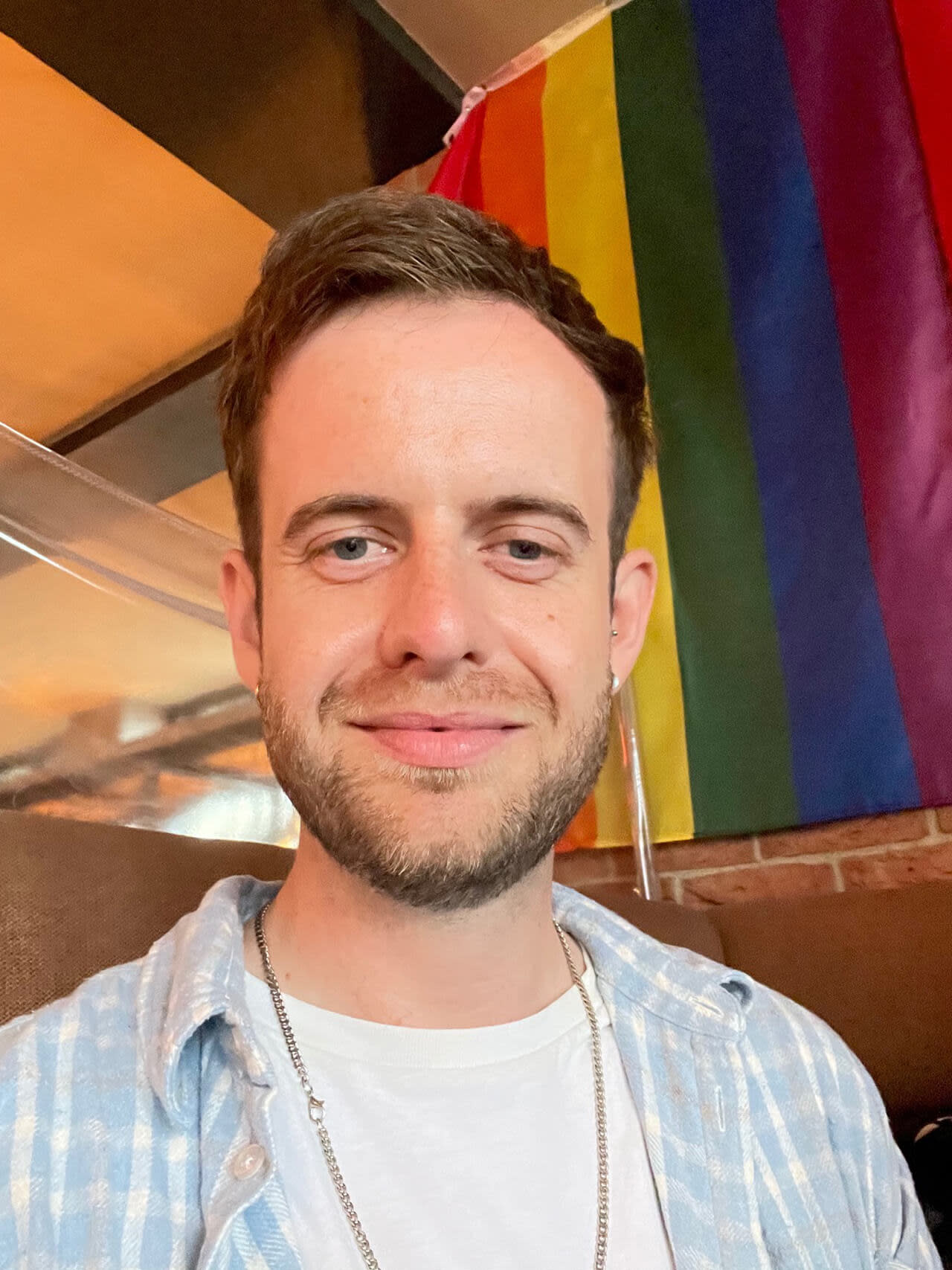 Photo of a man wearing a blue shirt, a rainbow flag behind him