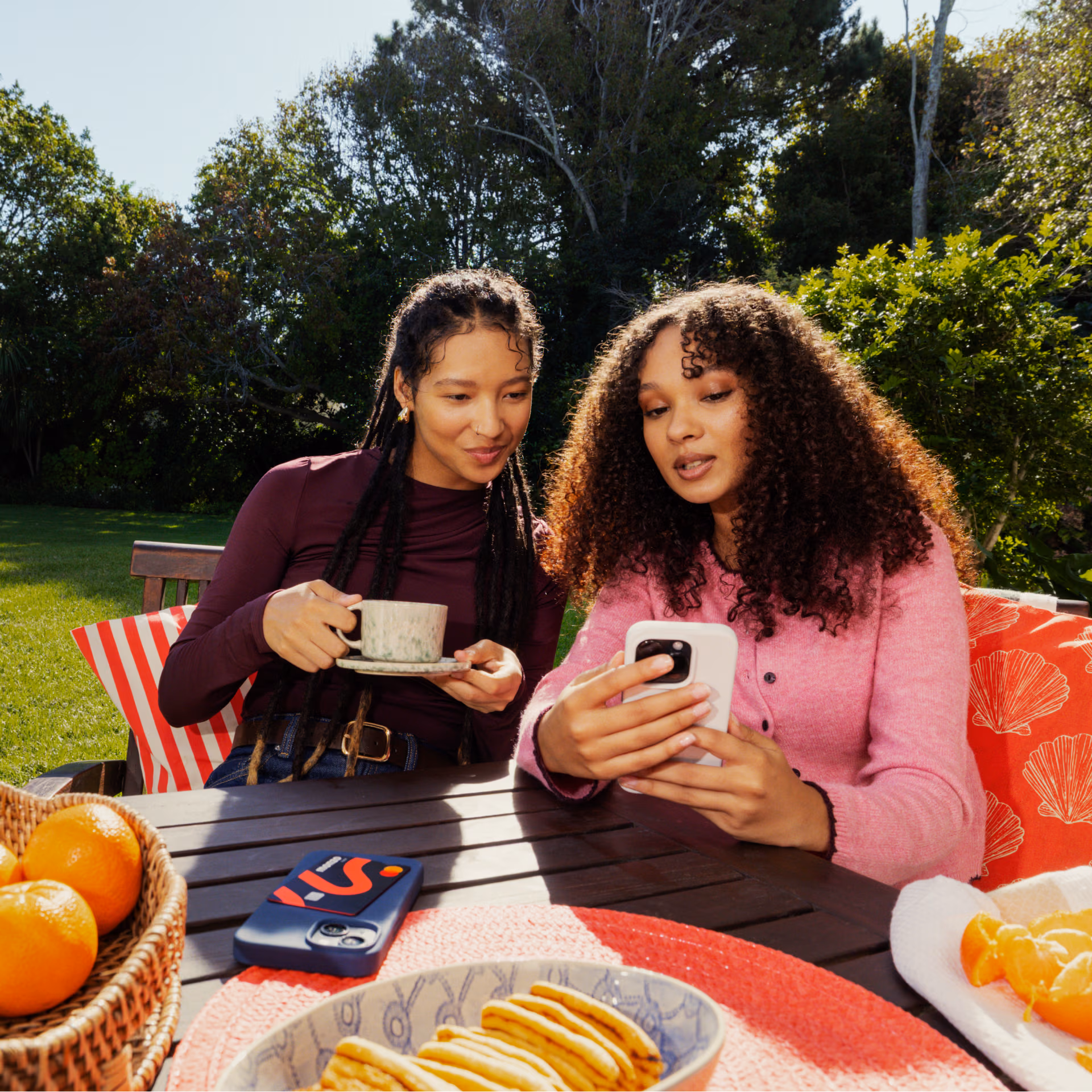 Two women sitting at a garden table looking at the Monzo app together on a phone.