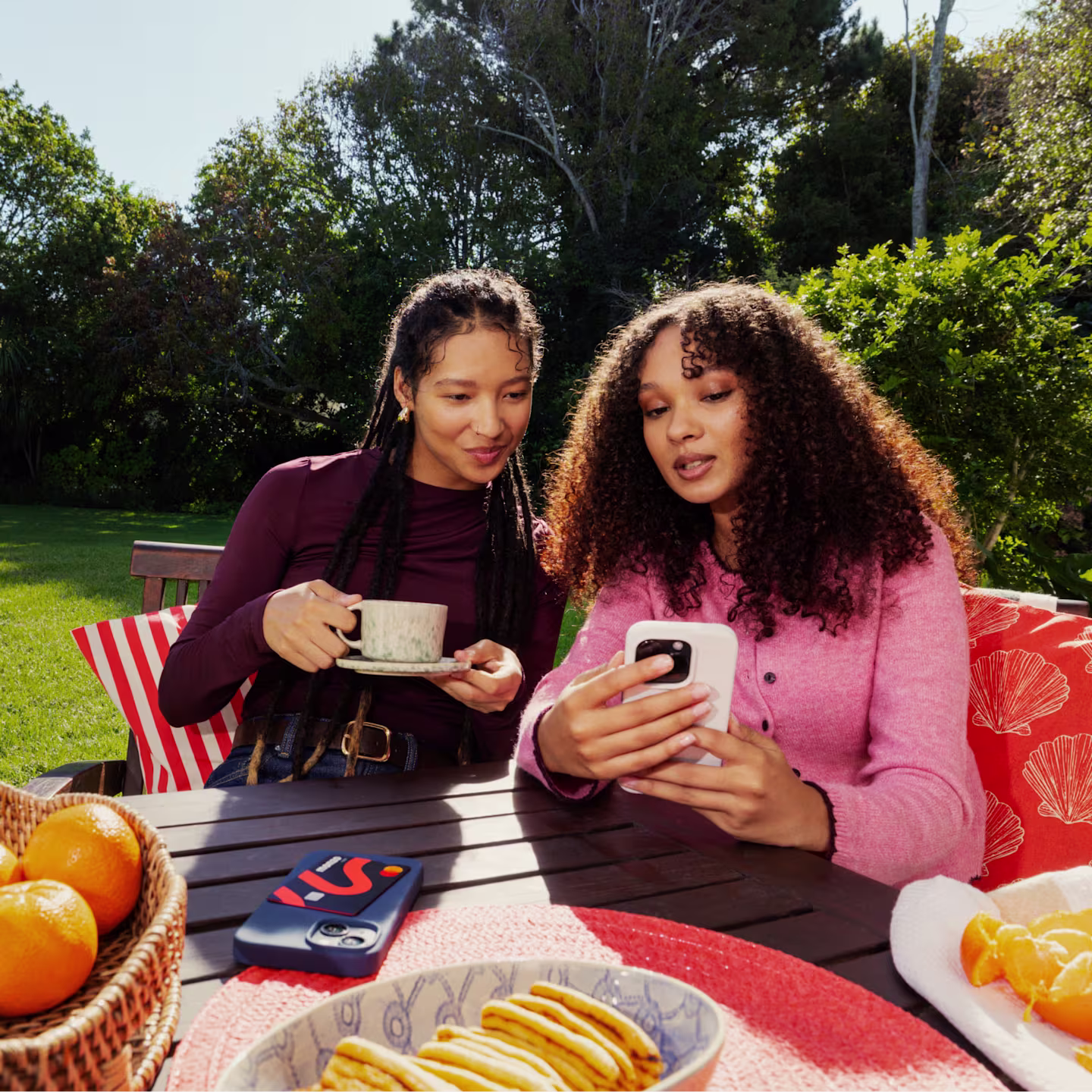 Two women sitting at a garden table looking at the Monzo app together on a phone.
