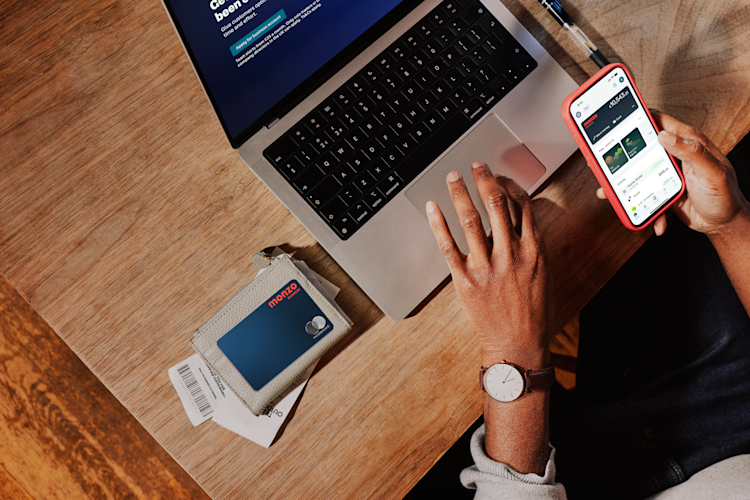 Overhead view of a business owner's workspace showing a laptop, phone displaying the Monzo app, and a Monzo business card in its holder on a wooden desk.