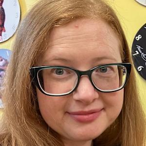 A closeup picture of Elizabeth Blakelock, Monzo's Accessibility and Inclusion Manager. She has long ginger hair, is smiling and wears black framed glasses.