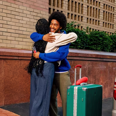 Two young adults hugging beside a suitcase outdoors.