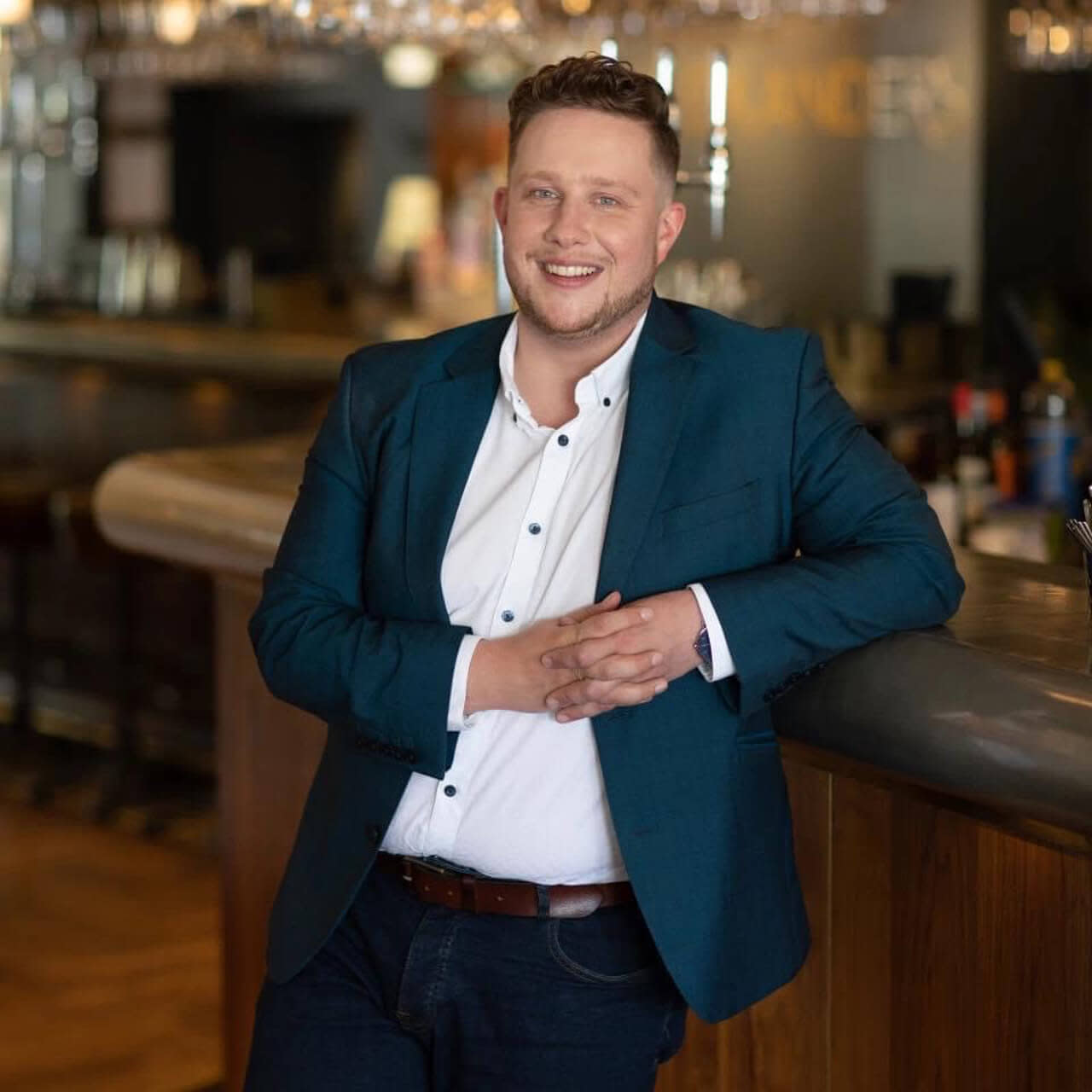 Man in a blazer, leaning against a bar