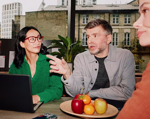 A man and two women having a discussion around a table with a laptop