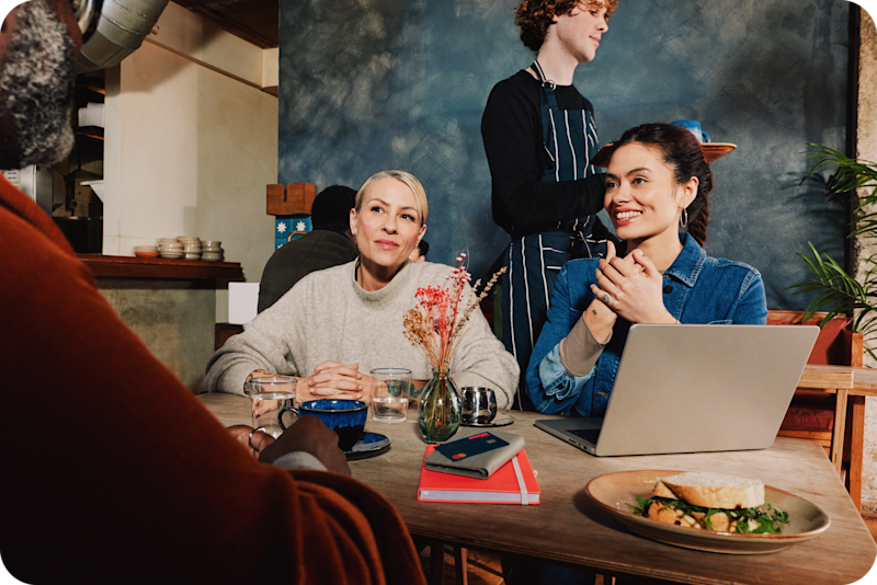 Overhead view of a business owner's workspace showing a laptop, phone displaying the Monzo app, and a Monzo business card in its holder on a wooden desk.
