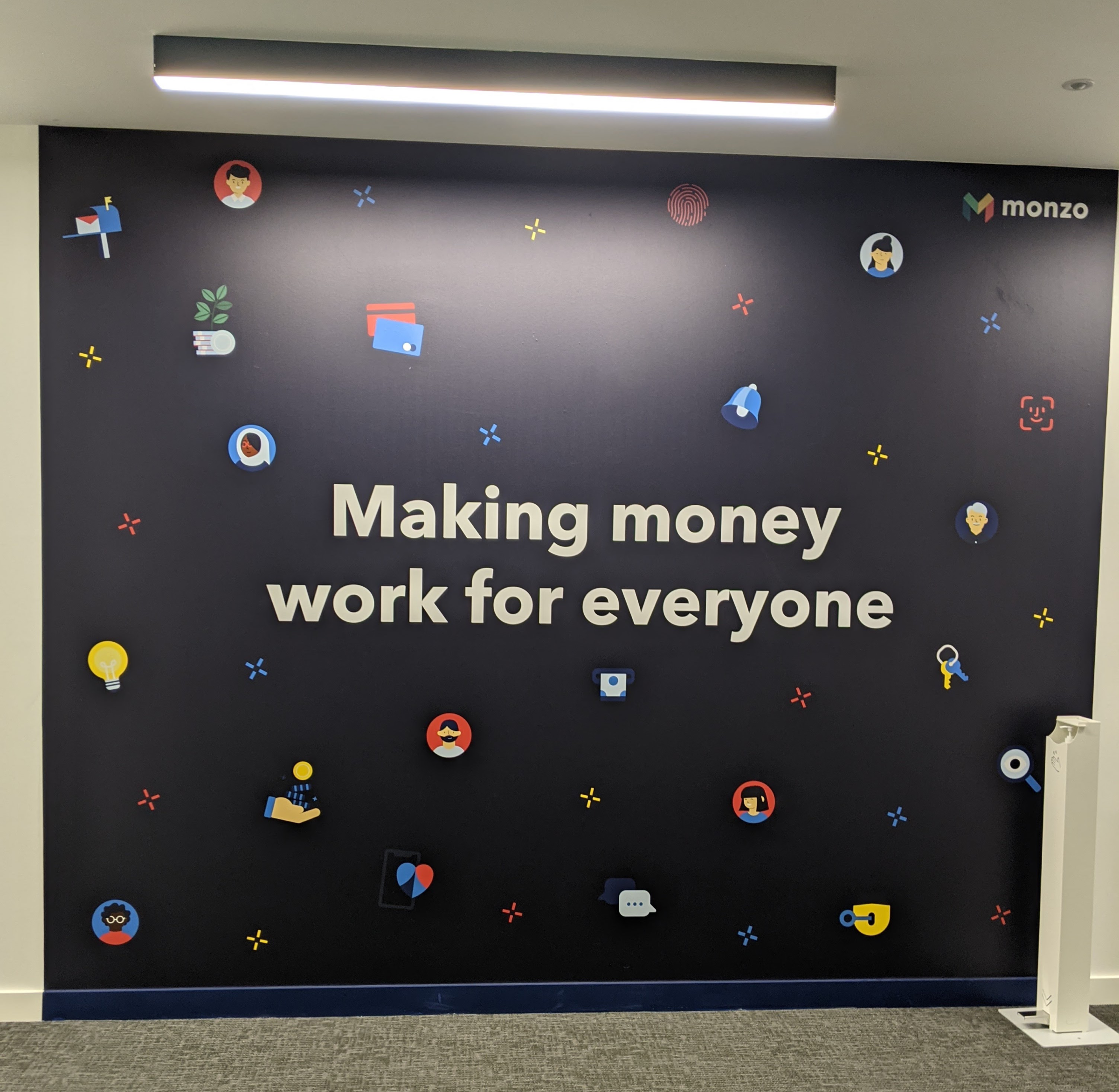 A sign in the Monzo office that says "making money work for everyone" surrounded by various money-related icons