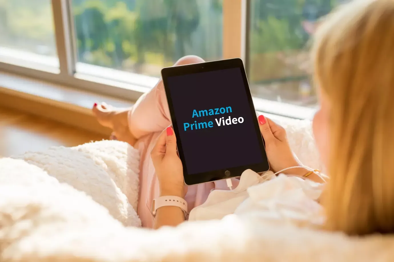 寝そべってタブレット端末でAazonPrimeVideoを見ている女性の写真