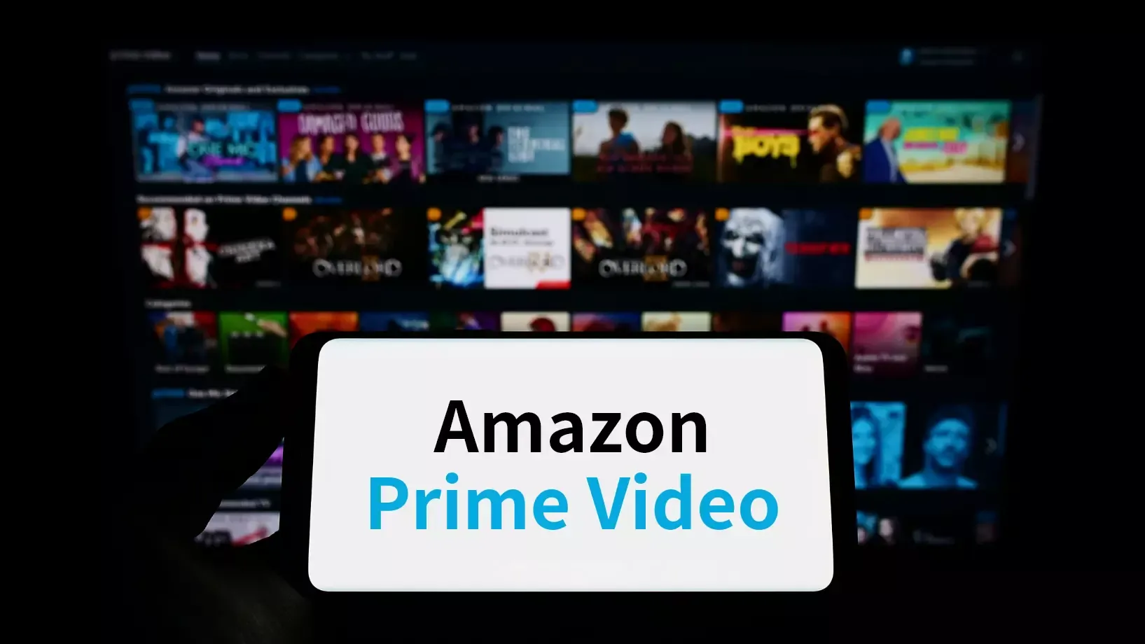 AmazonPrimeVideoのテキストが表示されたスマホとその奥に作品サムネイル画像が並ぶ写真