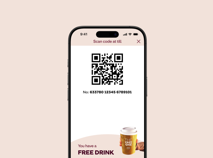 A smartphone screen displaying a QR code with the instruction "Scan code at till." Below the QR code is a number: "633780 12345 6789101." At the bottom, there is a promotional message stating "You have a FREE DRINK" accompanied by an image of a takeaway coffee cup.