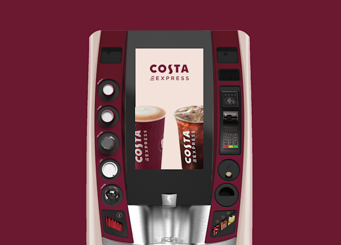 Costa Express self-service coffee machine with a large central touchscreen displaying two Costa cups — one with hot coffee and one with iced coffee. The machine features buttons and a card payment terminal on both sides, set against a maroon background.