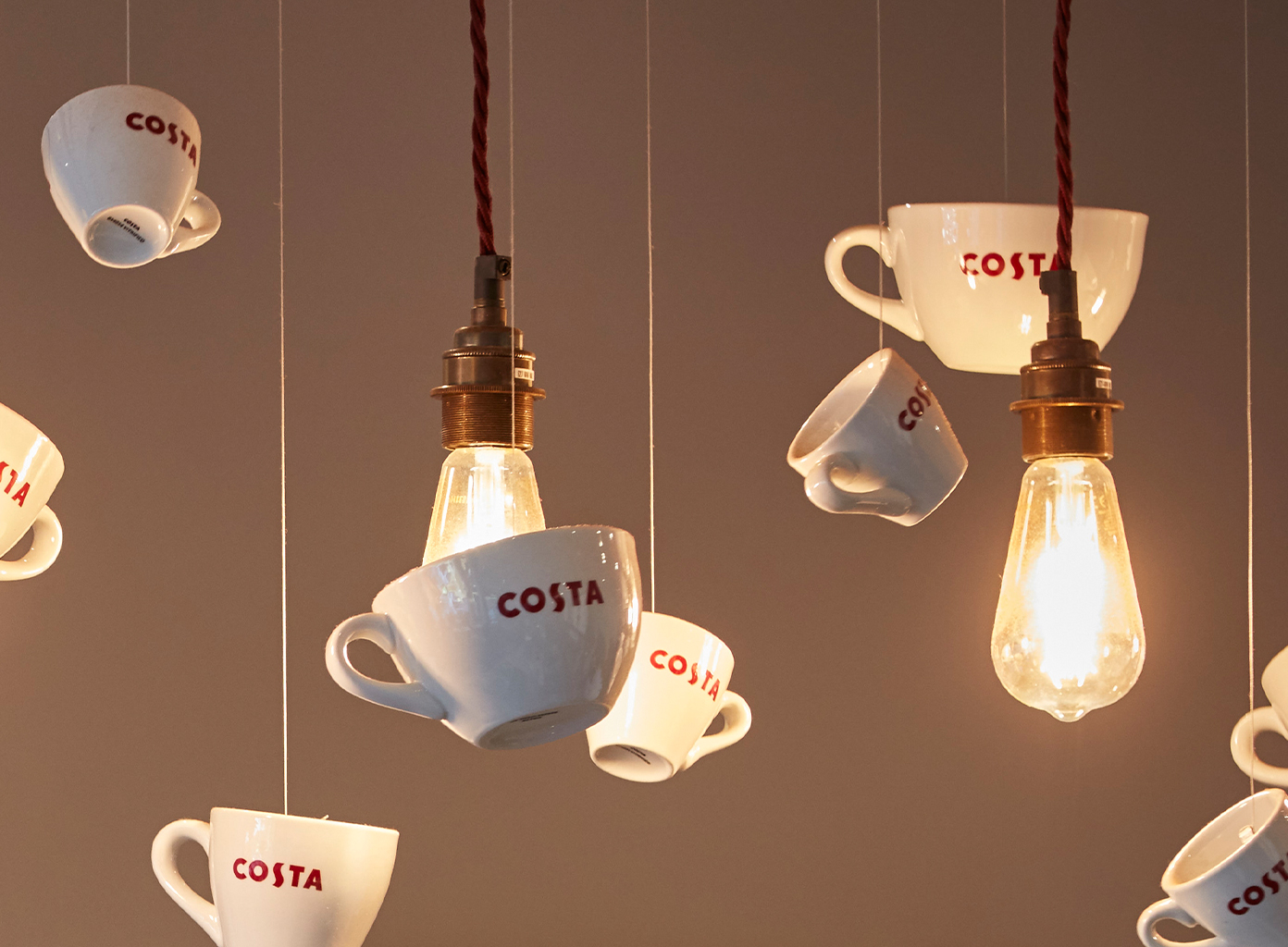 Costa Coffee ceramic cups suspended as décor around glowing vintage-style filament bulbs.