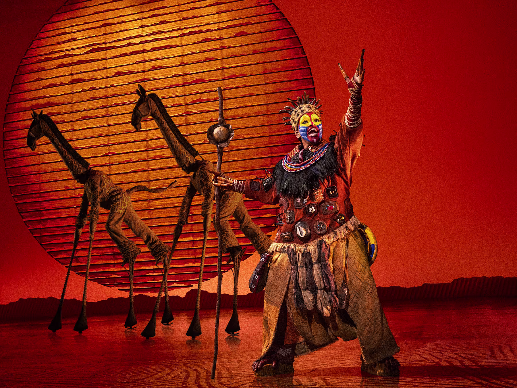 Rafiki posiert vor der aufgehenden Sonne, Giraffen im Hintergrund