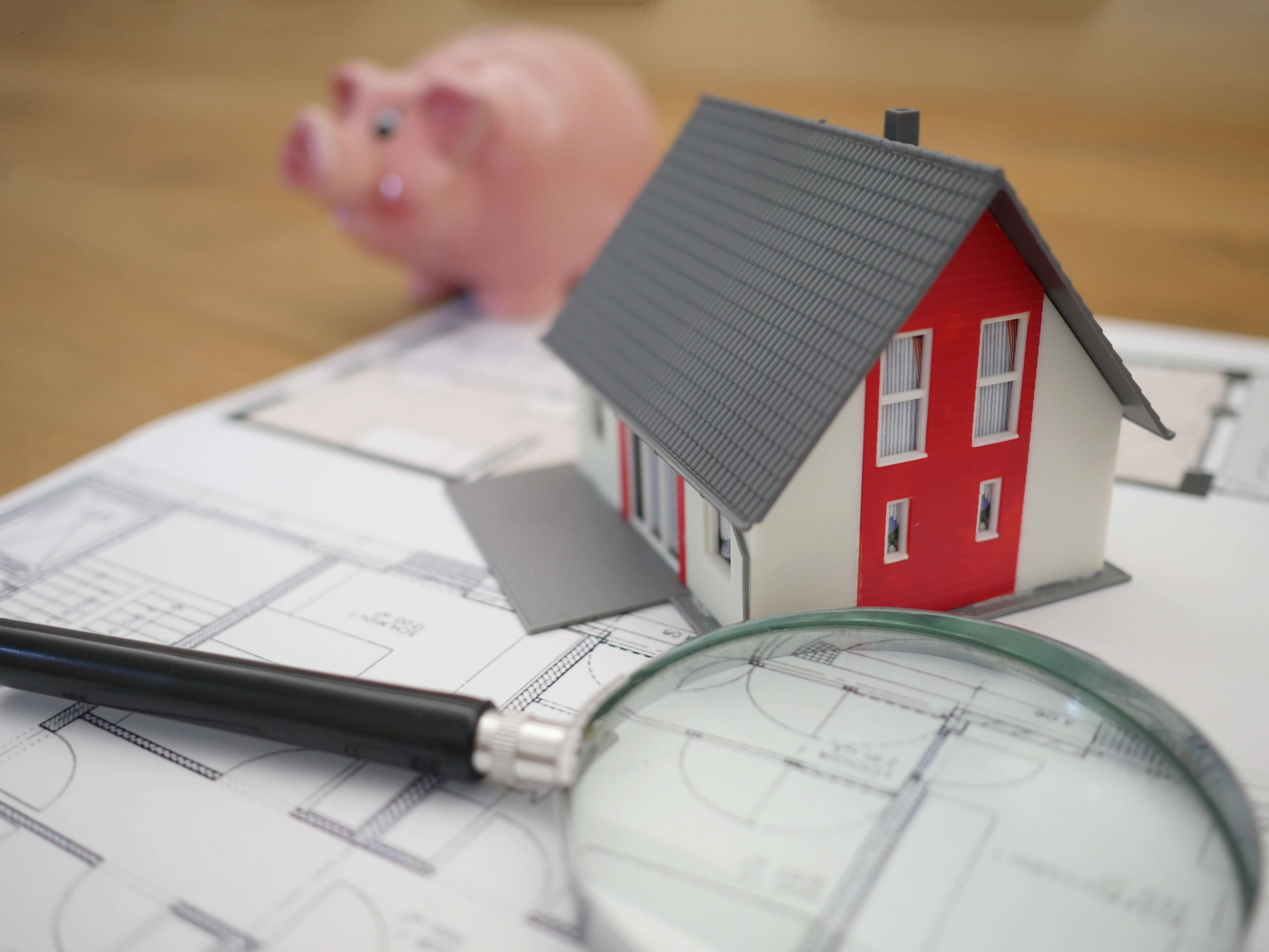 A floor plan with a magnifying glass, toy house and piggy bank placed on top