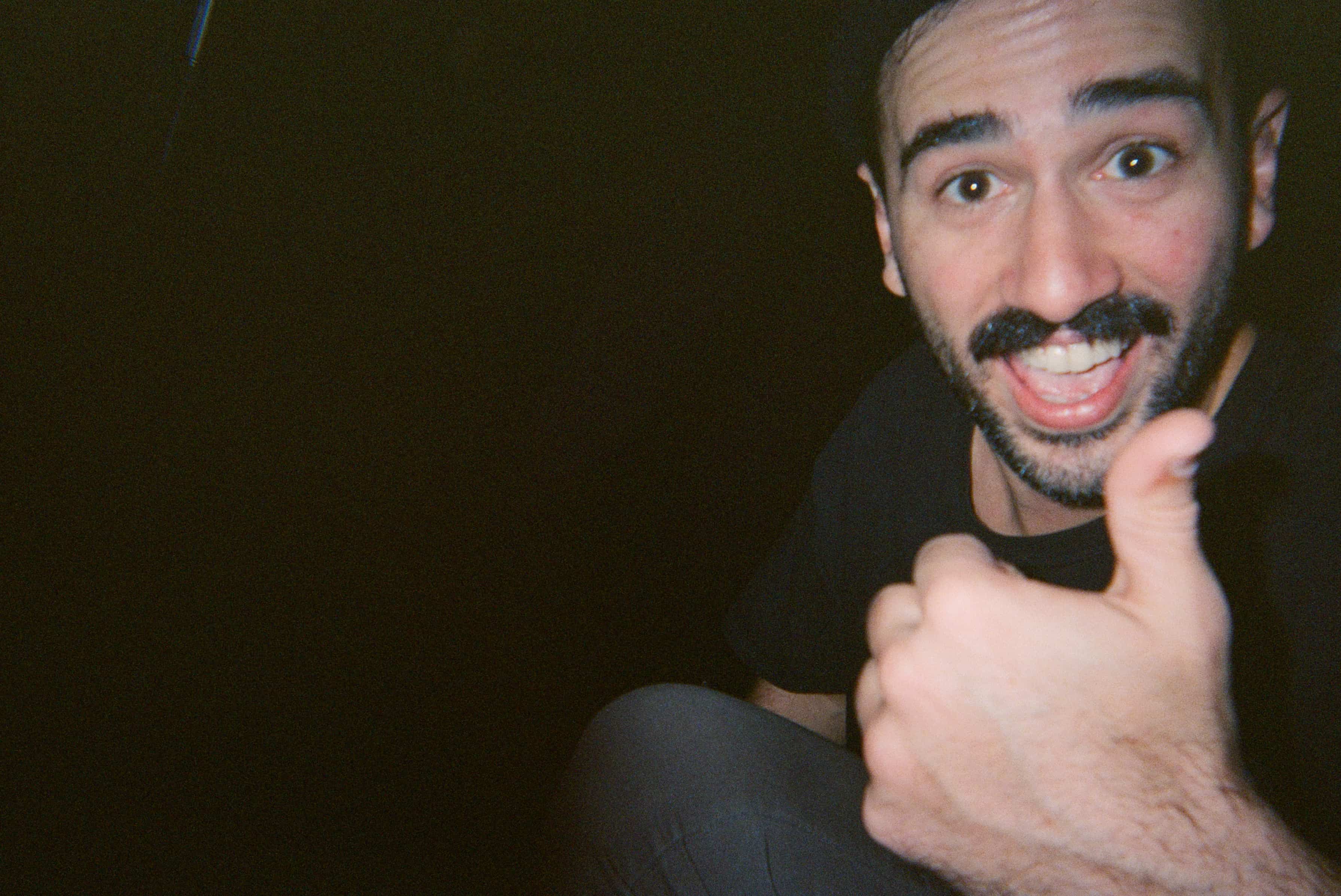 A man with mustache and beard smiling and giving thumbs up.