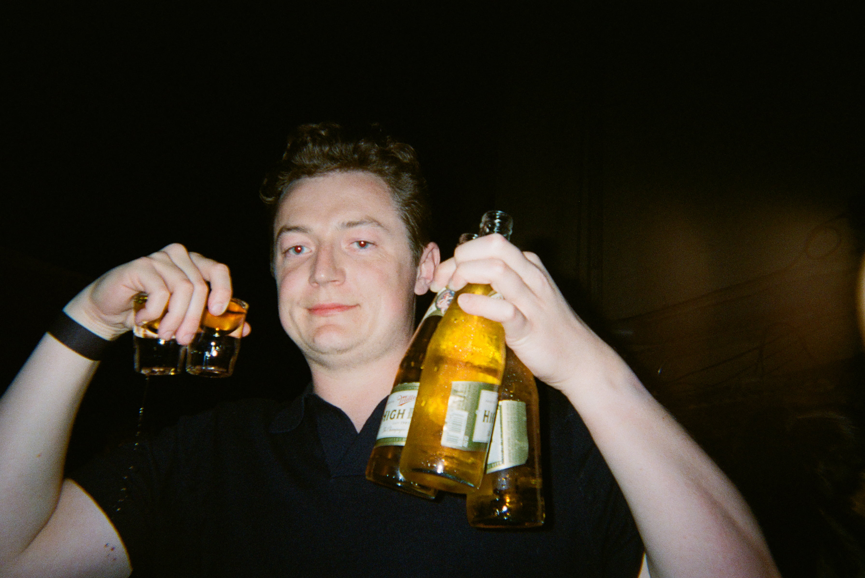 A person holding bottles of beer and shots of whiskey.