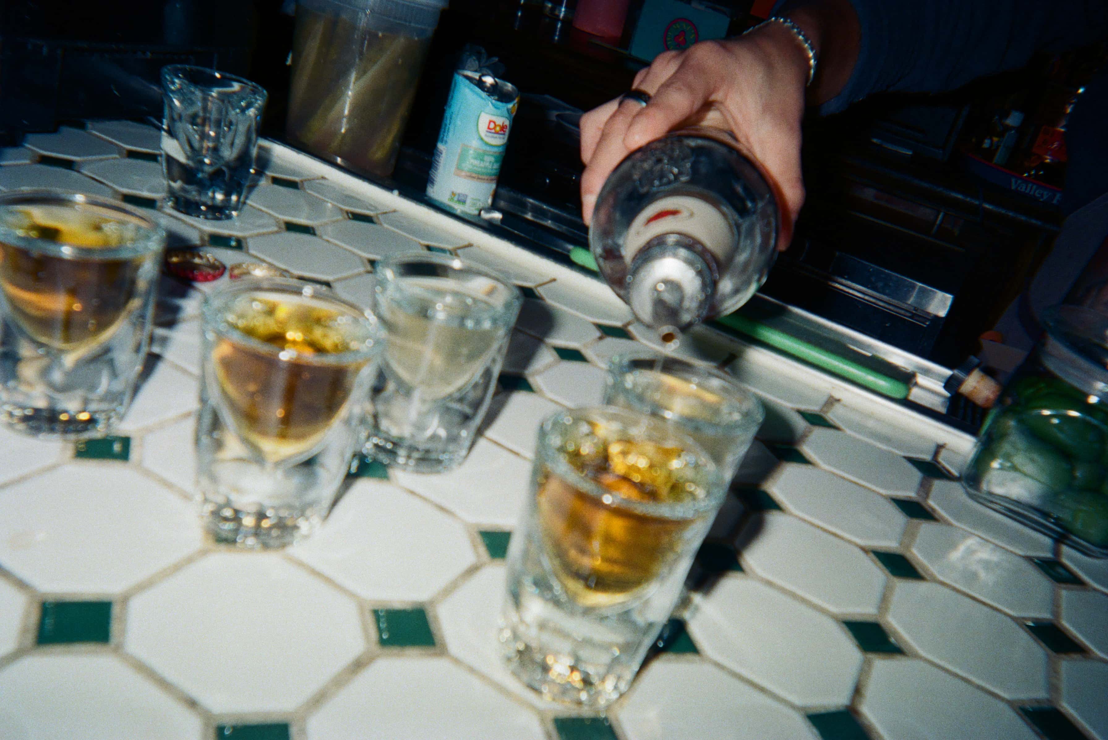 A hand pouring a drink into shot glasses.
