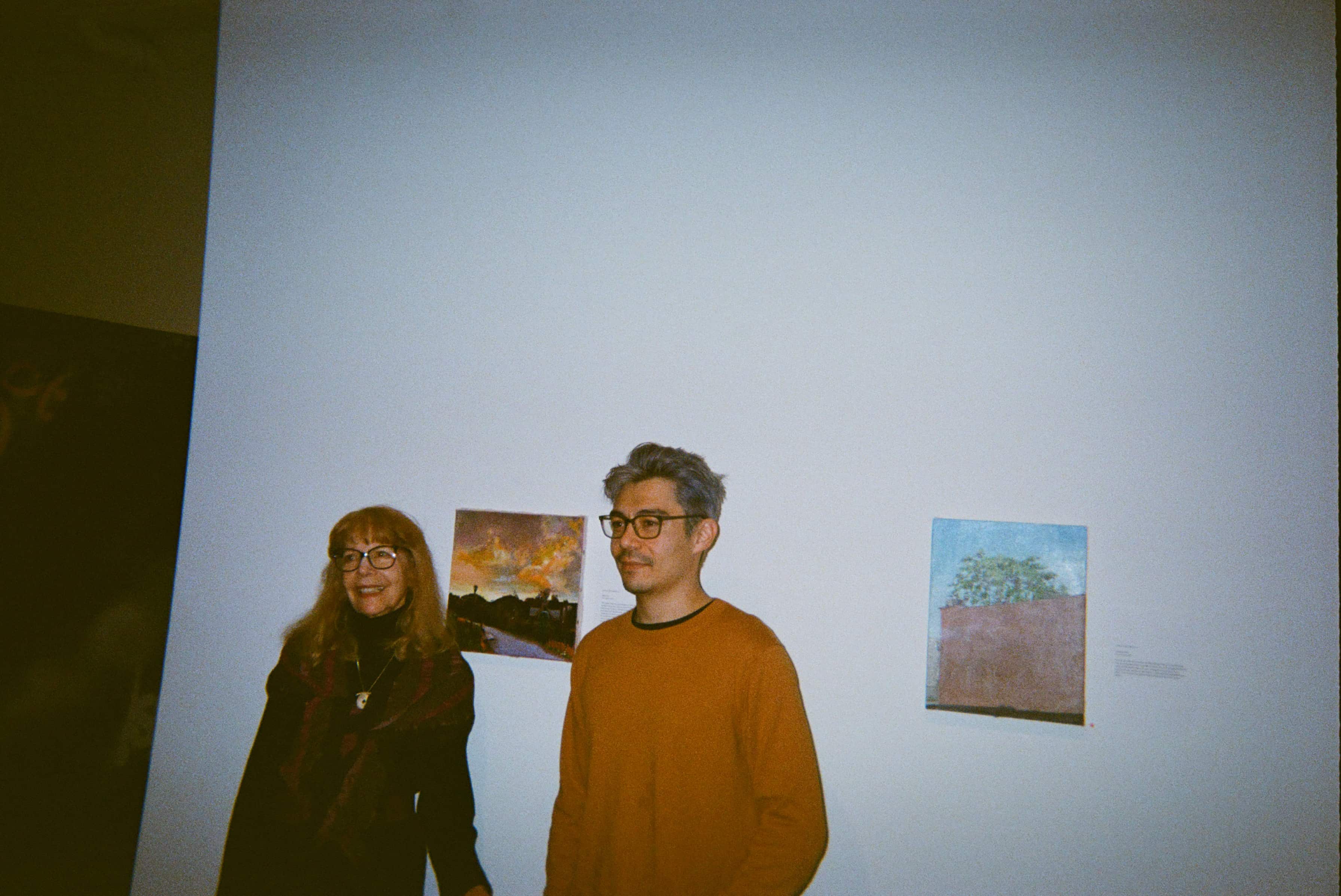 Two people standing in front of a wall with paintings.