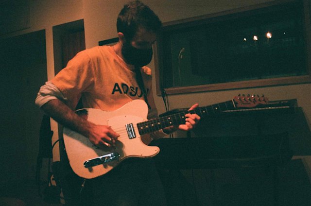 Masked person in a recording studio playing electric guitar.