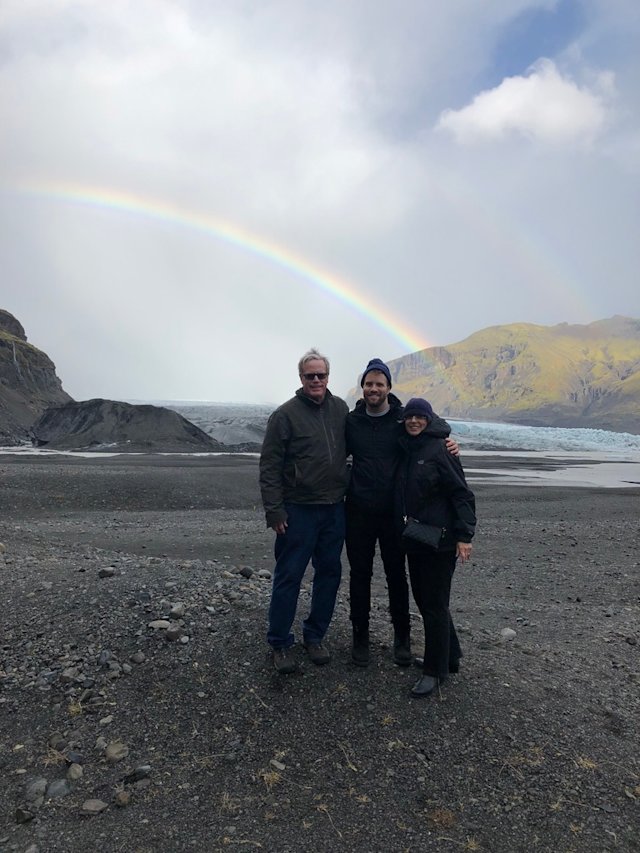 Three people standing before a glacier and a rainbow in Iceland.