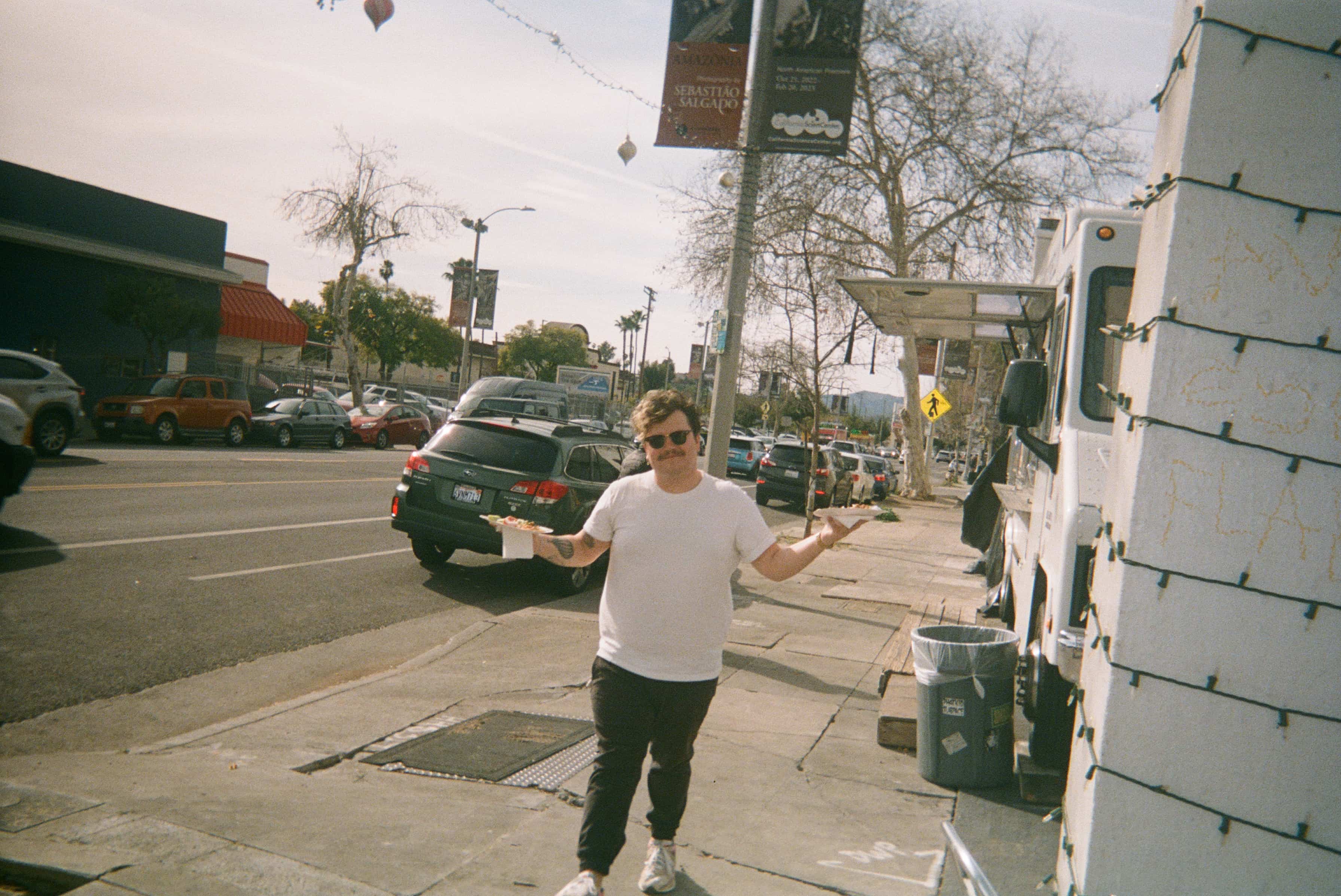 A person standing on a sidewalk holding food from a food truck.