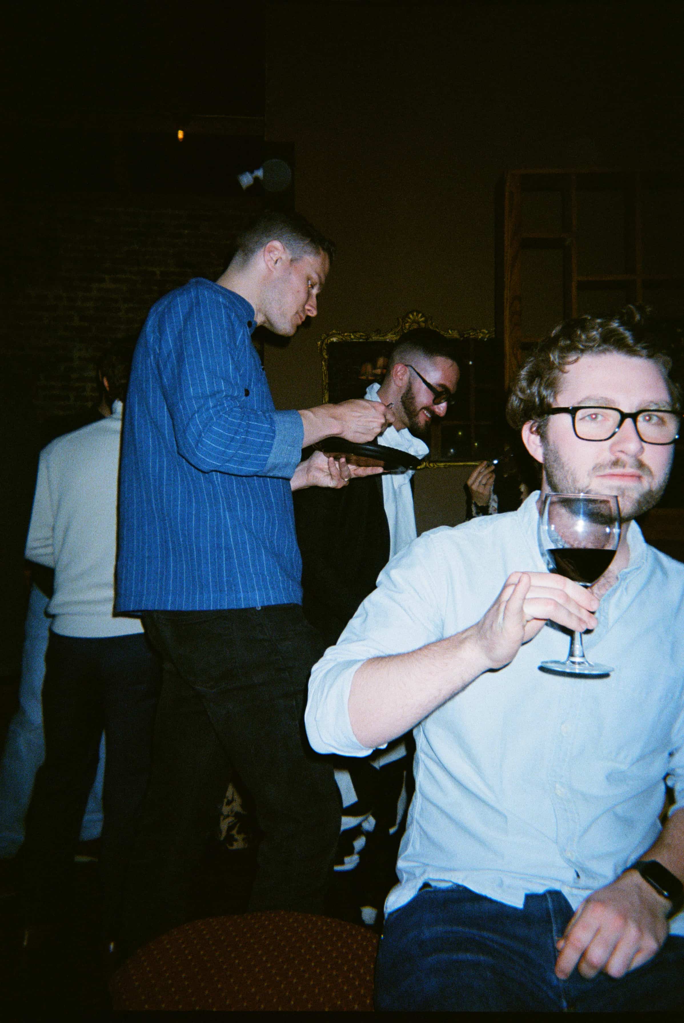 A group of men standing around a table with a glass of wine.