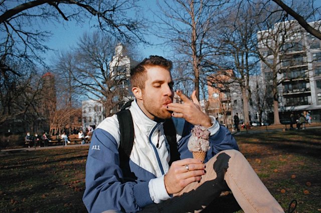Person seated on the grass in a park eating ice cream.
