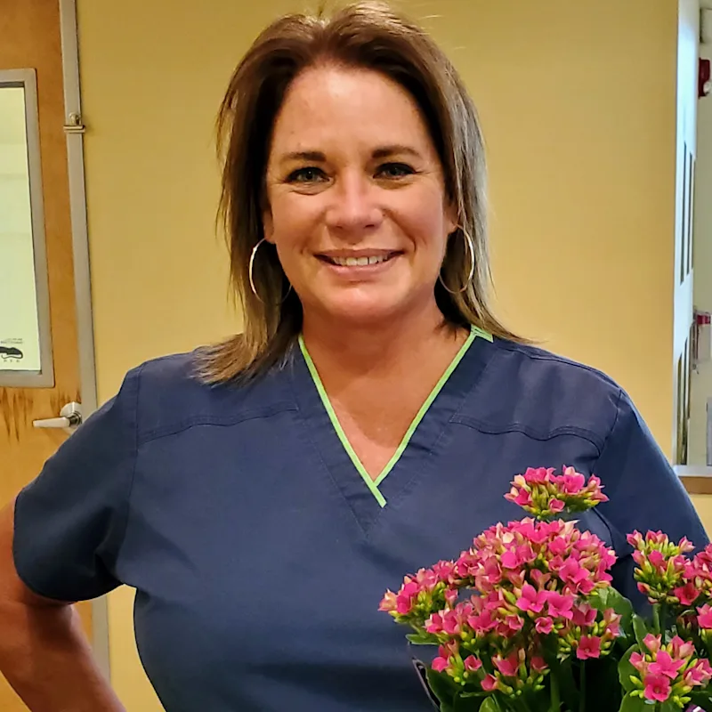 Cara Longshore smiling inside next to a bouquet of pink flowers. Cara Longshore smiling inside next to a bouquet of pink flowers.