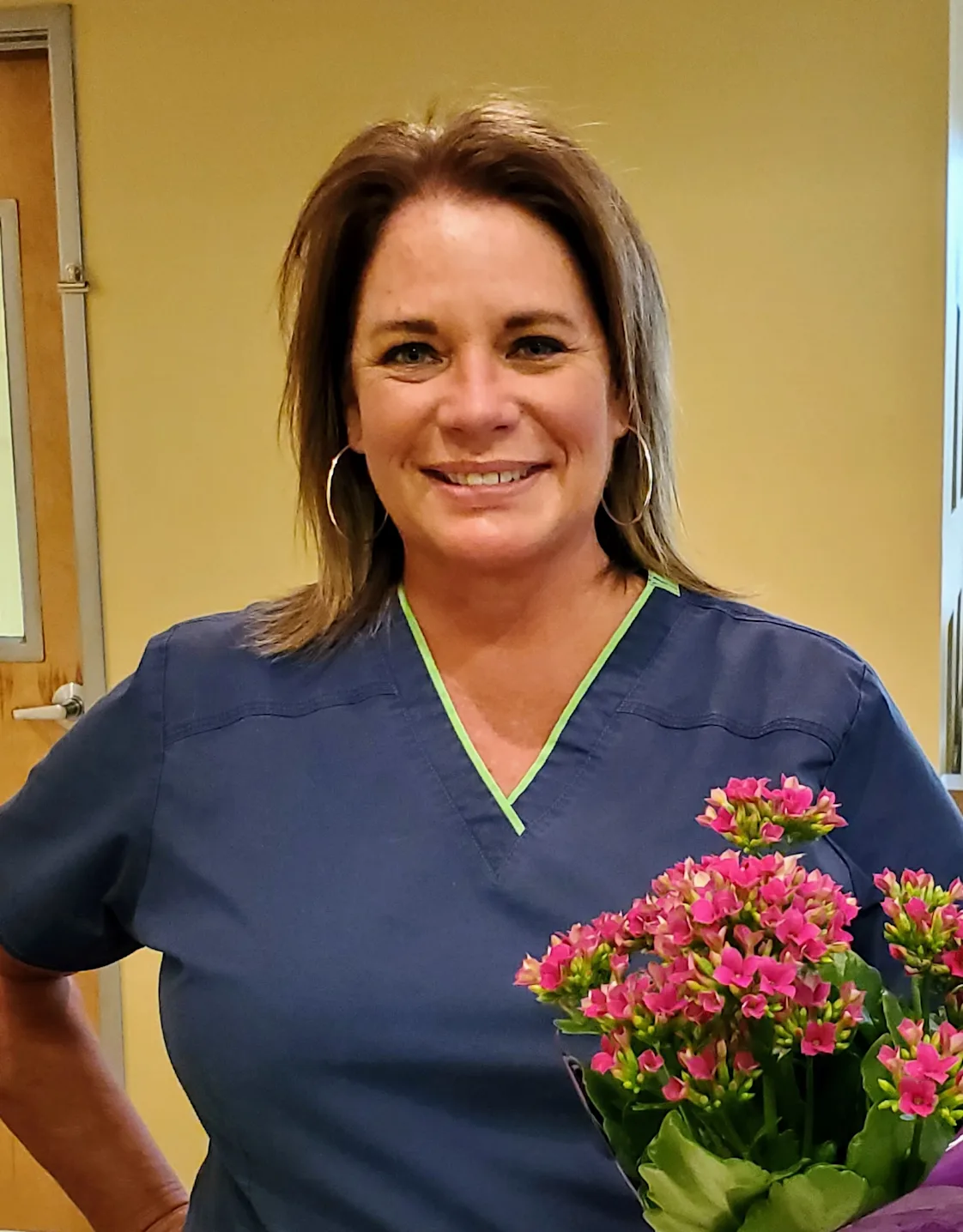 Cara Longshore smiling inside next to a bouquet of pink flowers. Cara Longshore smiling inside next to a bouquet of pink flowers.