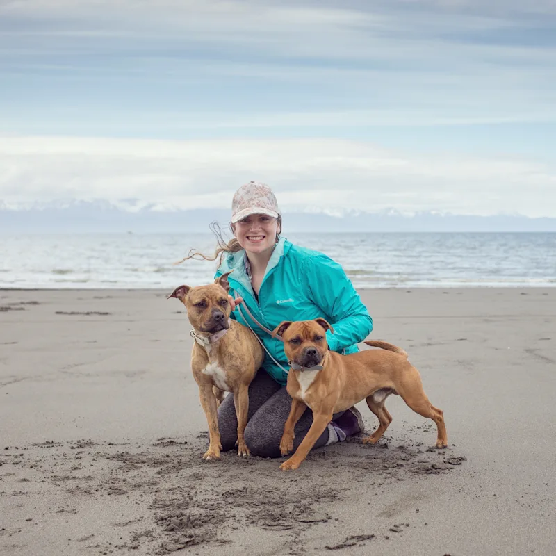 Elora's staff photo from Alaska Veterinary Clinic where she is at a beach with her two brown dogs smiling. Elora's staff photo from Alaska Veterinary Clinic where she is at a beach with her two brown dogs smiling.