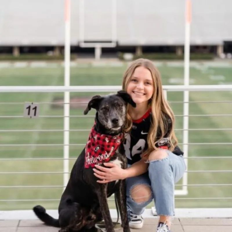 Dr. Justine Gordner holding onto a dog in front of a football field. Dr. Justine Gordner holding onto a dog in front of a football field.
