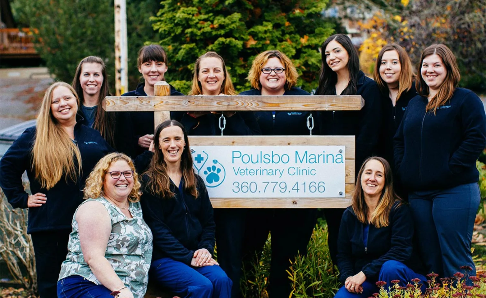 Poulsbo Marina Veterinary Clinic is posing for a group photo outside and next to their clinic's sign. There's eleven women in the picture. Poulsbo Marina Veterinary Clinic is posing for a group photo outside and next to their clinic's sign. There's eleven women in the picture.