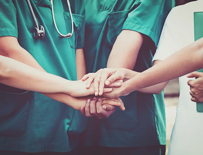 Photo of hospital staff having hands on top of one another to show team work Photo of hospital staff having hands on top of one another to show team work